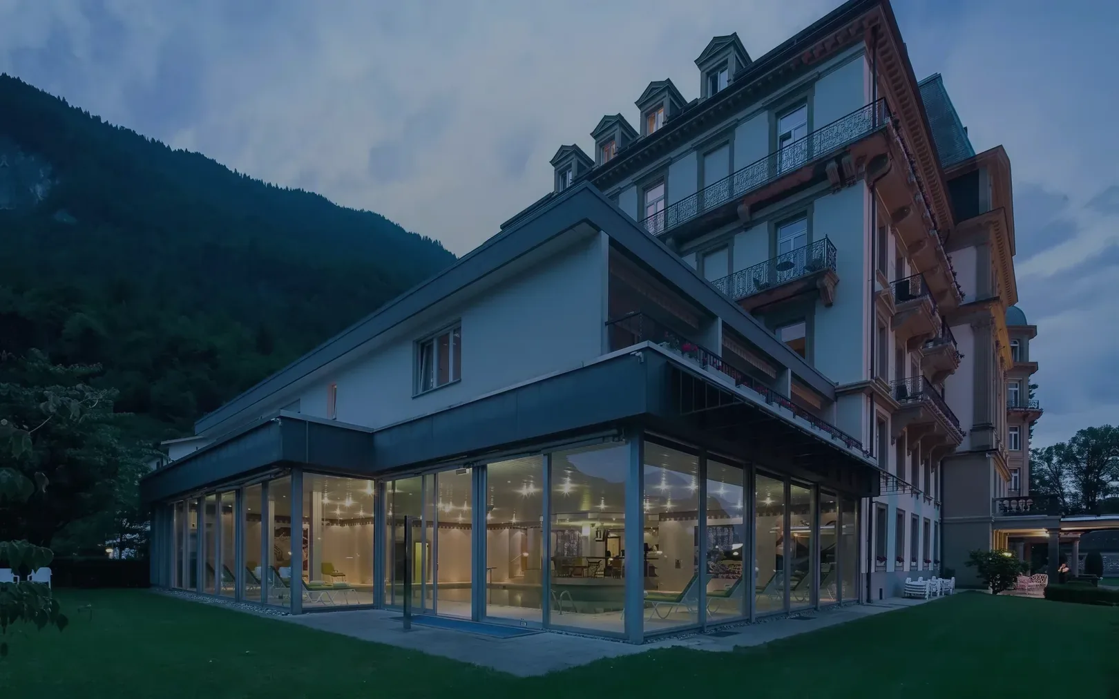 Der Glasbau des La Vallée SPA am Abend, dahinter das Haus
