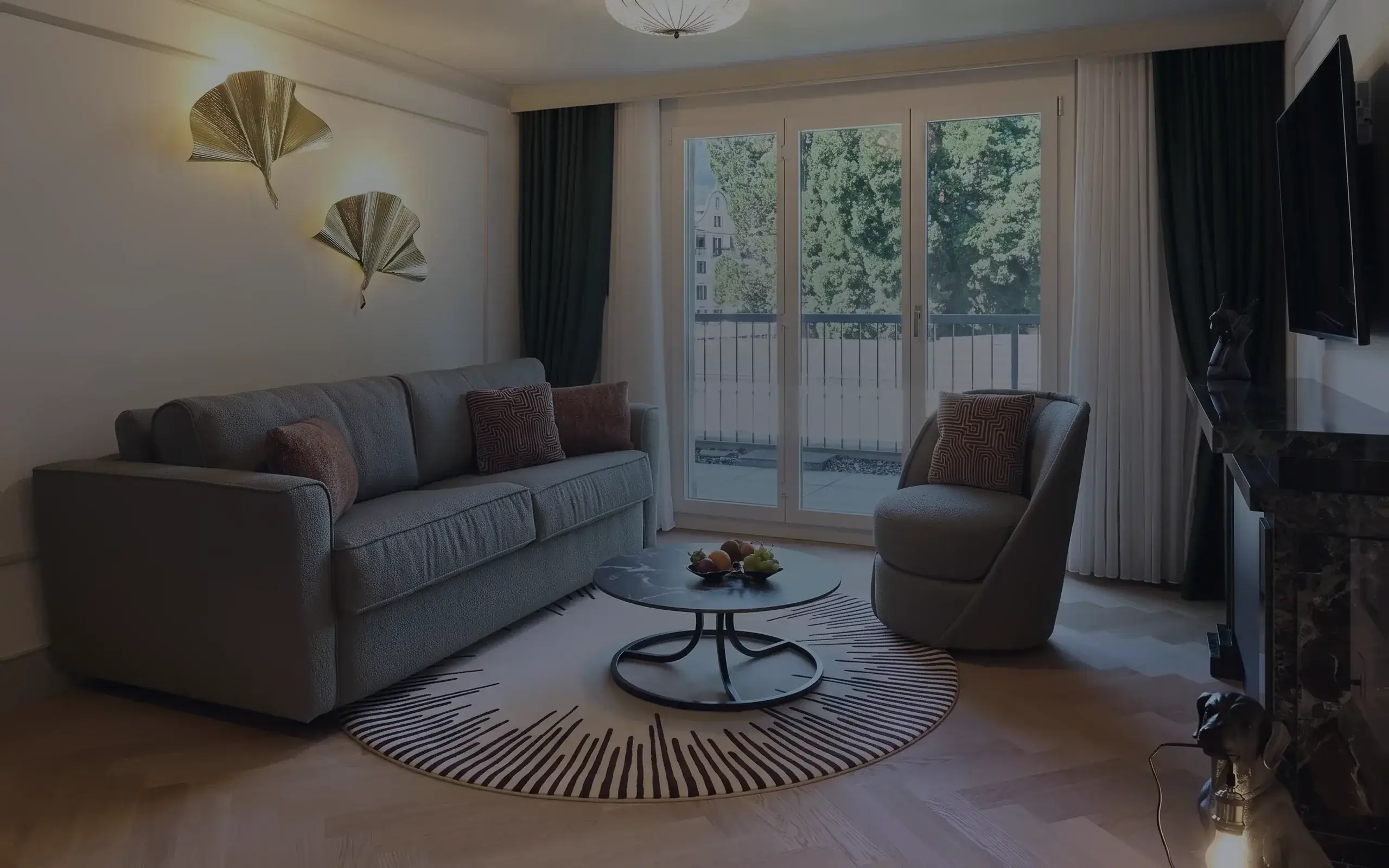 Der Wohnbereich der Interlaken Suite mit Sofa, goldenen Wandleuchten und Balkontür