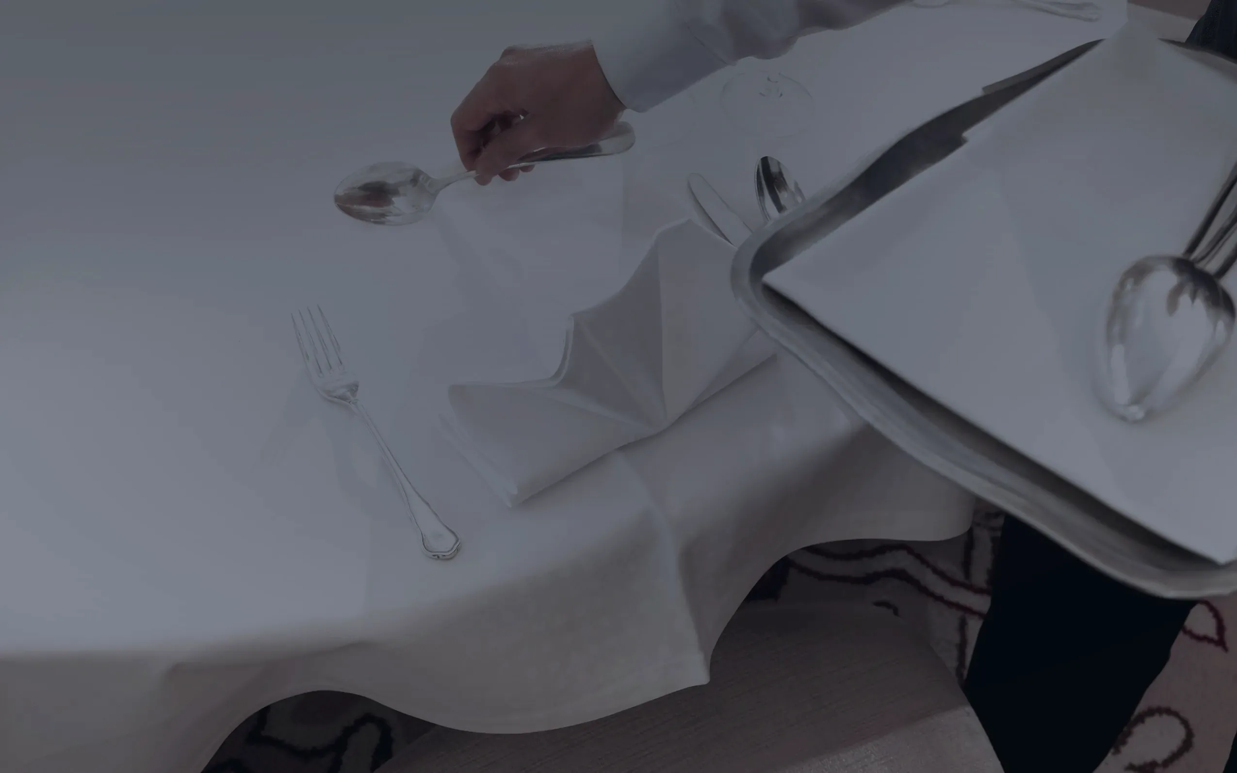 Ein Kellner legt die Serviette, Silberbesteck auf weissem Tischtuch