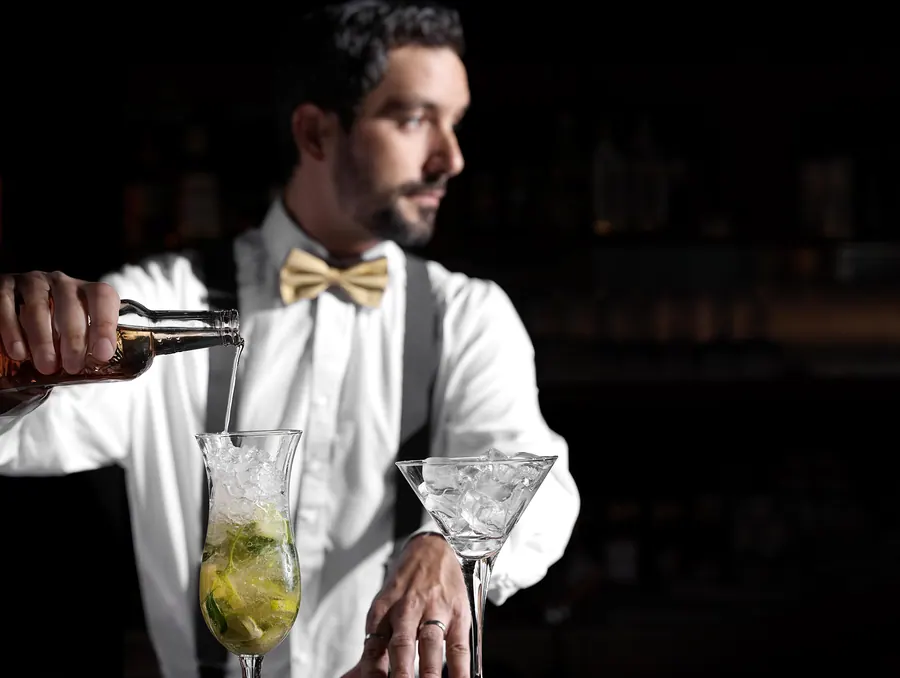 Der Barkeeper mit Fliege giesst einen Drink auf, in der Bar «Le Vieux Rivage»