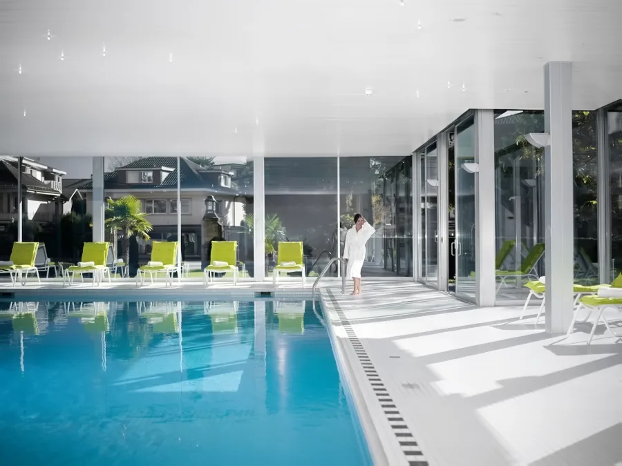 Das Schwimmbad im Sonnenlicht, ein Gast im Bademantel, dahinter der Garten